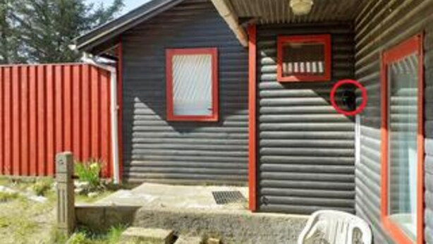 Une cabane en bois avec une porte rouge, une petite fenêtre et une fenêtre encadrée de rouge.