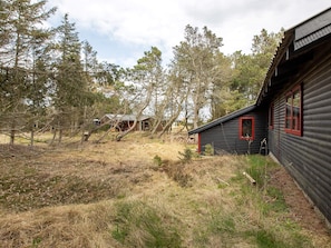 A rustic cabin with a black exterior and red trim, surrounded by trees and a grassy field. - Comely Holiday Home in Thisted near Beach (Thisted)