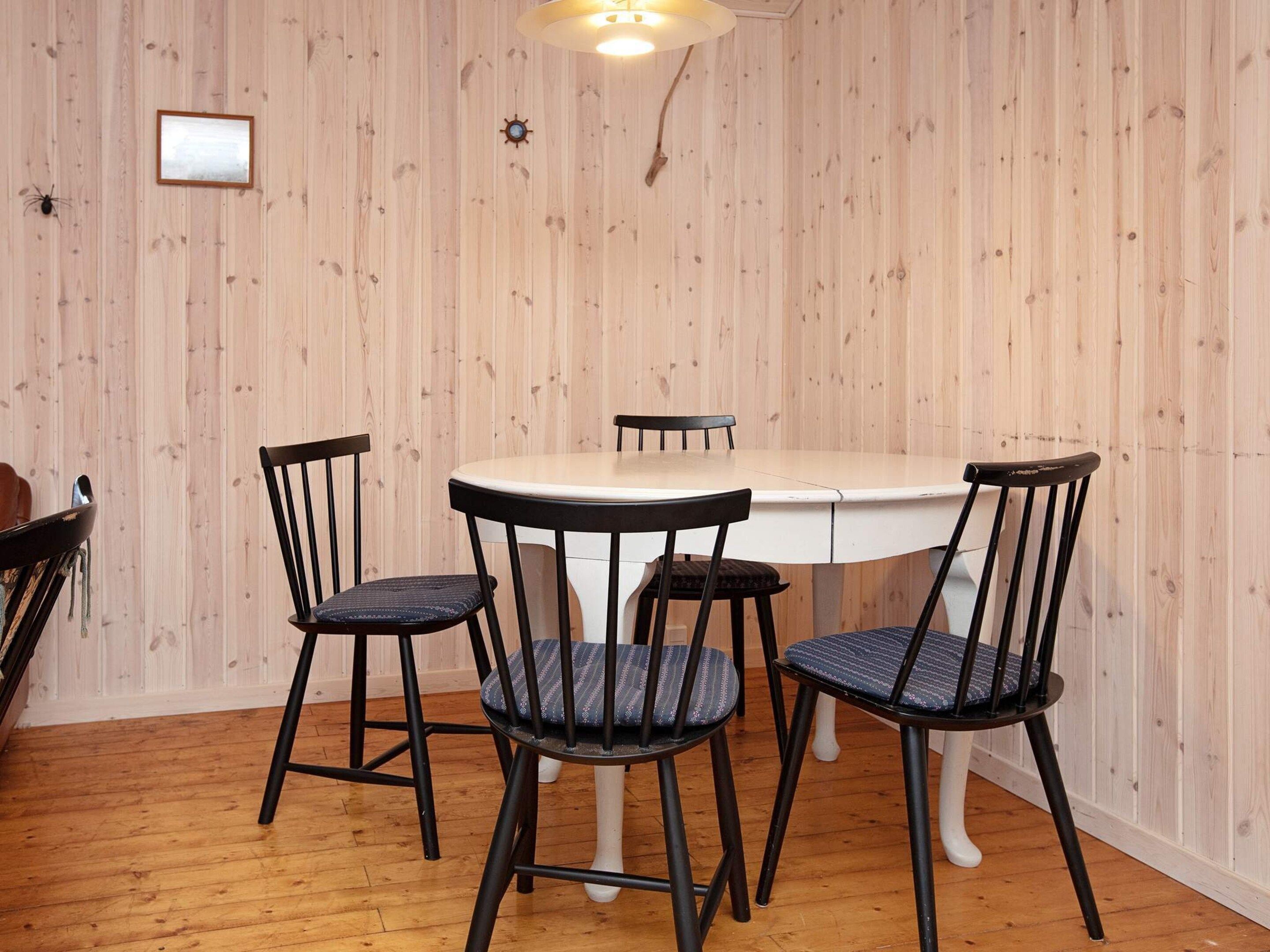 A dining area with a round table and four chairs, wooden walls, and a wooden floor.