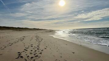 Een strand met voetafdrukken die naar het water leiden, een heldere lucht en een lage zon aan de horizon.