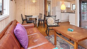 Un intérieur chaleureux avec un plafond en bois, un canapé agrémenté d’un coussin violet, une table à manger avec des chaises et un coin cuisine.