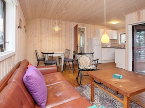 Un intérieur chaleureux avec un plafond en bois, un canapé agrémenté d’un coussin violet, une table à manger avec des chaises et un coin cuisine.