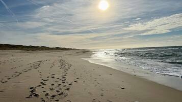 A beach with footprints leading to the water, a clear sky, and the sun low on the horizon.