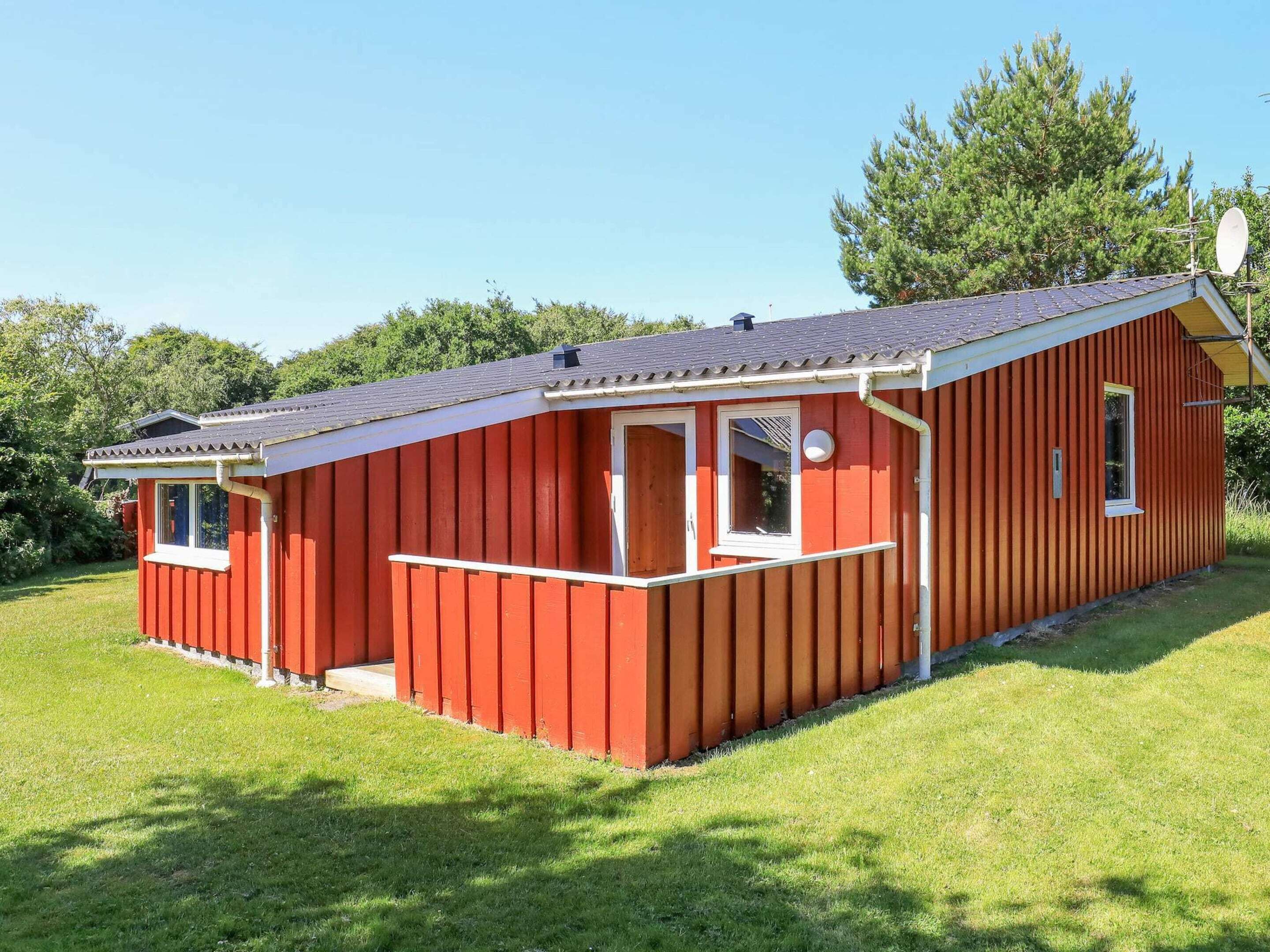 Een rode houten chalet met een schuin dak, een schotelantenne en een klein terras.
