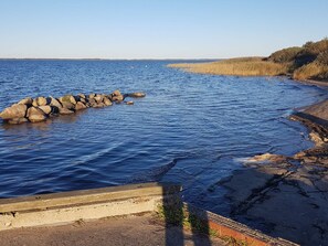 A coastal landscape with a rocky shoreline, calm water, and a distant view of wind turbines.