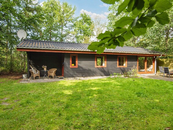 A log cabin with a covered porch, a small outdoor seating area, and a grassy yard.