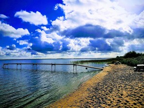 A beach with a wooden pier extending into calm waters, a sandy shore, and a cloudy sky.