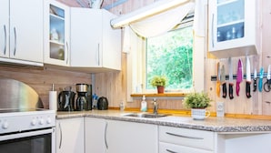 A modern kitchen with white cabinets, a stove, a sink, and a window with a view of greenery. - Pleasant Holiday Home in Silkeborg near Lake (Silkeborg)