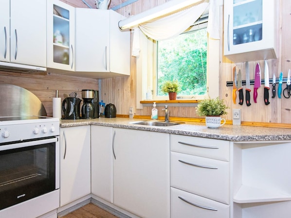 A modern kitchen with white cabinets, a stove, a sink, and a window with a view of greenery. - Pleasant Holiday Home in Silkeborg near Lake (Silkeborg)