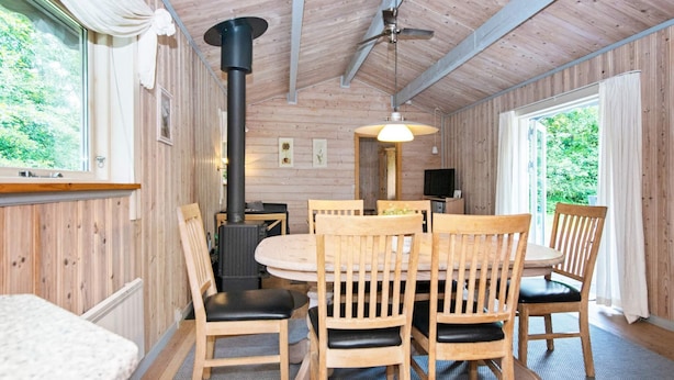 A wooden interior with a round dining table, four chairs, a ceiling fan, and a large window. - Pleasant Holiday Home in Silkeborg near Lake (Silkeborg)