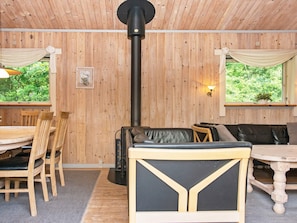 Une pièce chaleureuse aux murs en bois, dotée d’un système de chauffage central, d’un coin repas avec des chaises et une table, et d’un espace détente avec un canapé et des coussins.