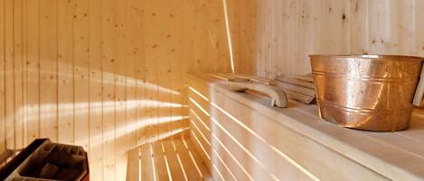 Una sauna con bancos de madera y un cubo de cobre.