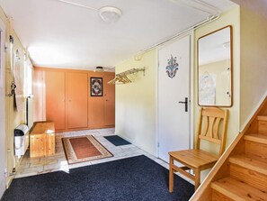 Un couloir avec une porte en bois, un porte-manteau, une chaise et un escalier.