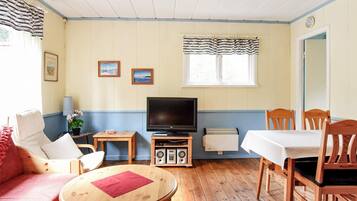 A room with a television, a table, a sofa, and a dining table with chairs.