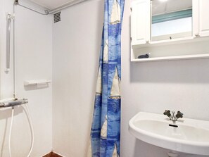 Une salle de bain avec un lavabo blanc, une douche et un rideau de douche orné d’un motif de voilier.