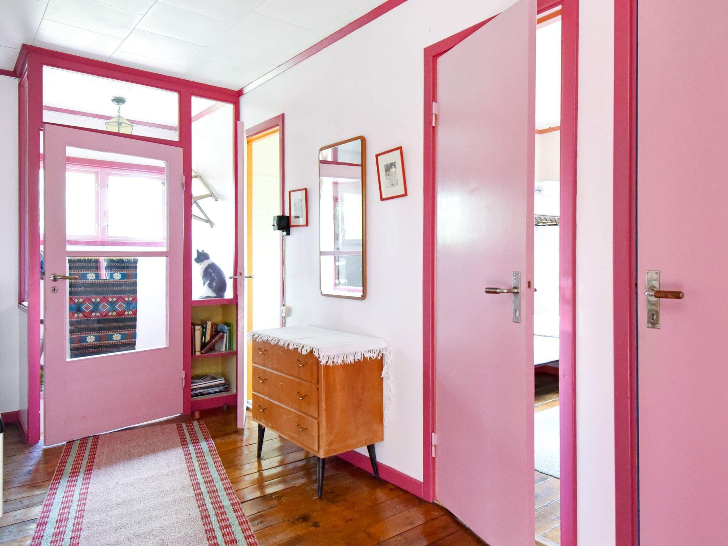 A room with pink walls, a wooden dresser, a mirror, and a door leading outside.