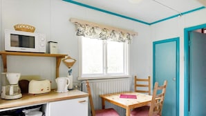 A compact kitchen with a microwave, toaster, and kettle on the counter, a small dining table with chairs, and a window with a decorative valance. - 8 Person Holiday Home in Salen (Salen)