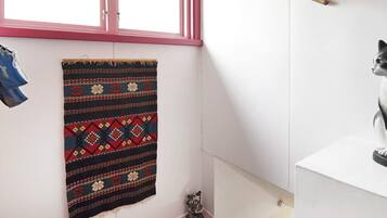 A bathroom with a window, a hanging towel, a drying rack, and a cat statue.