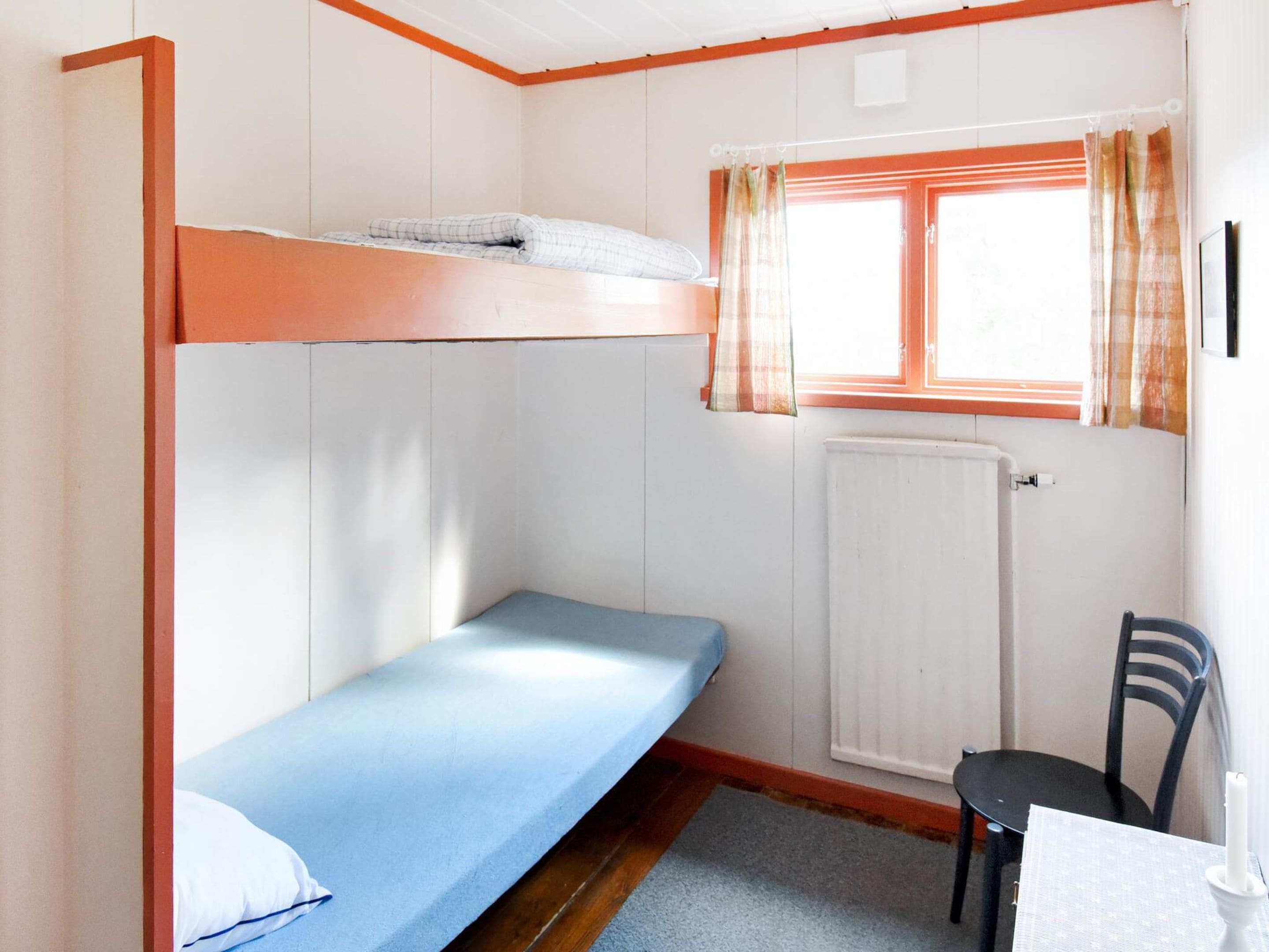 Habitació amb lliteres, un llit individual, taula, cadira i finestra amb cortines.