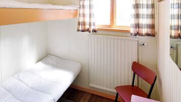 A small, single-room accommodation with a bunk bed, a chair, a table, and a window with curtains.