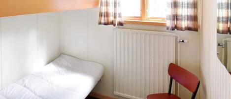 Un petit logement d’une seule pièce, comprenant un lit superposé, une chaise, une table et une fenêtre avec des rideaux.