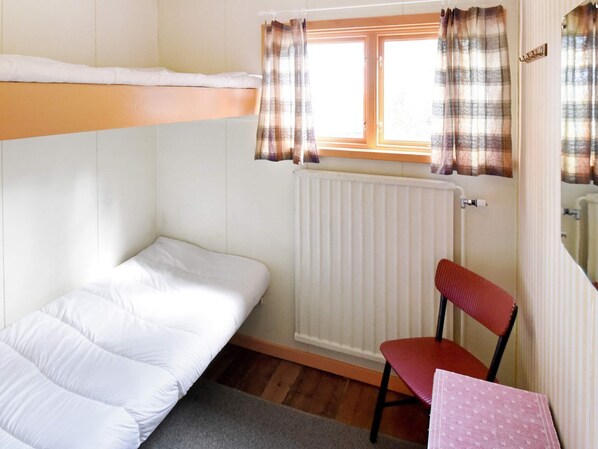 A small, single-room accommodation with a bunk bed, a chair, a table, and a window with curtains.