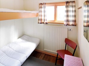 A small, single-room accommodation with a bunk bed, a chair, a table, and a window with curtains.