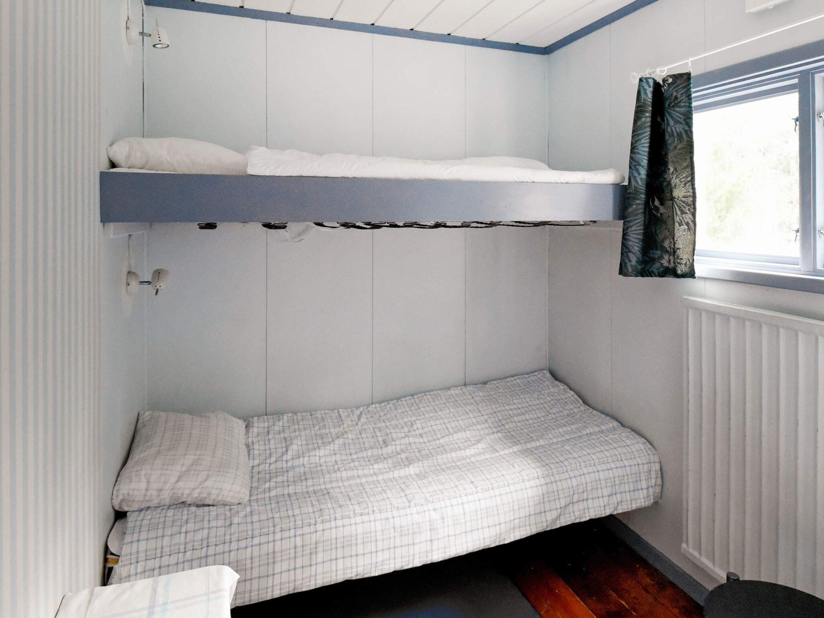 A compact room with a bunk bed and a single bed, a window with curtains, and a radiator.