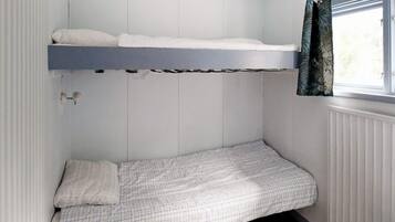 A compact room with a bunk bed and a single bed, a window with curtains, and a radiator.