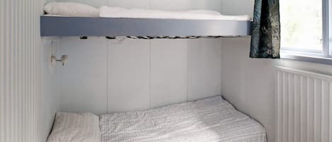 Une petite chambre avec un lit superposé et un lit simple, une fenêtre avec des rideaux et un radiateur.