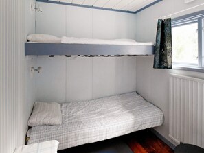 Une petite chambre avec un lit superposé et un lit simple, une fenêtre avec des rideaux et un radiateur.