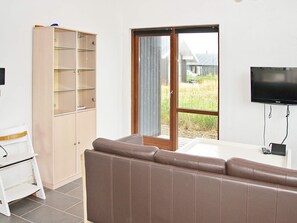 Una habitación con un sofá marrón, un aparador de madera con estantes de vidrio, una puerta corrediza de cristal y un televisor montado en la pared.
