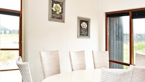 A dining area with a round table and six chairs, two framed floral paintings on the wall, and large windows with a view of greenery. - 8 Person Holiday Home in Ulfborg (Ulfborg)