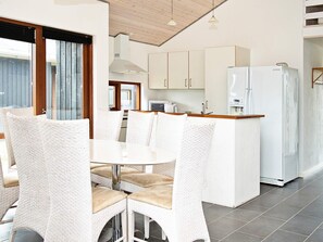 Una cocina moderna con armarios blancos, refrigerador empotrado y comedor con sillas de mimbre y una mesa blanca.
