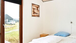 A bedroom with a bed, a small bedside table, a wall-mounted power outlet, and a window with a view of a car and buildings outside. - 8 Person Holiday Home in Ulfborg (Ulfborg)