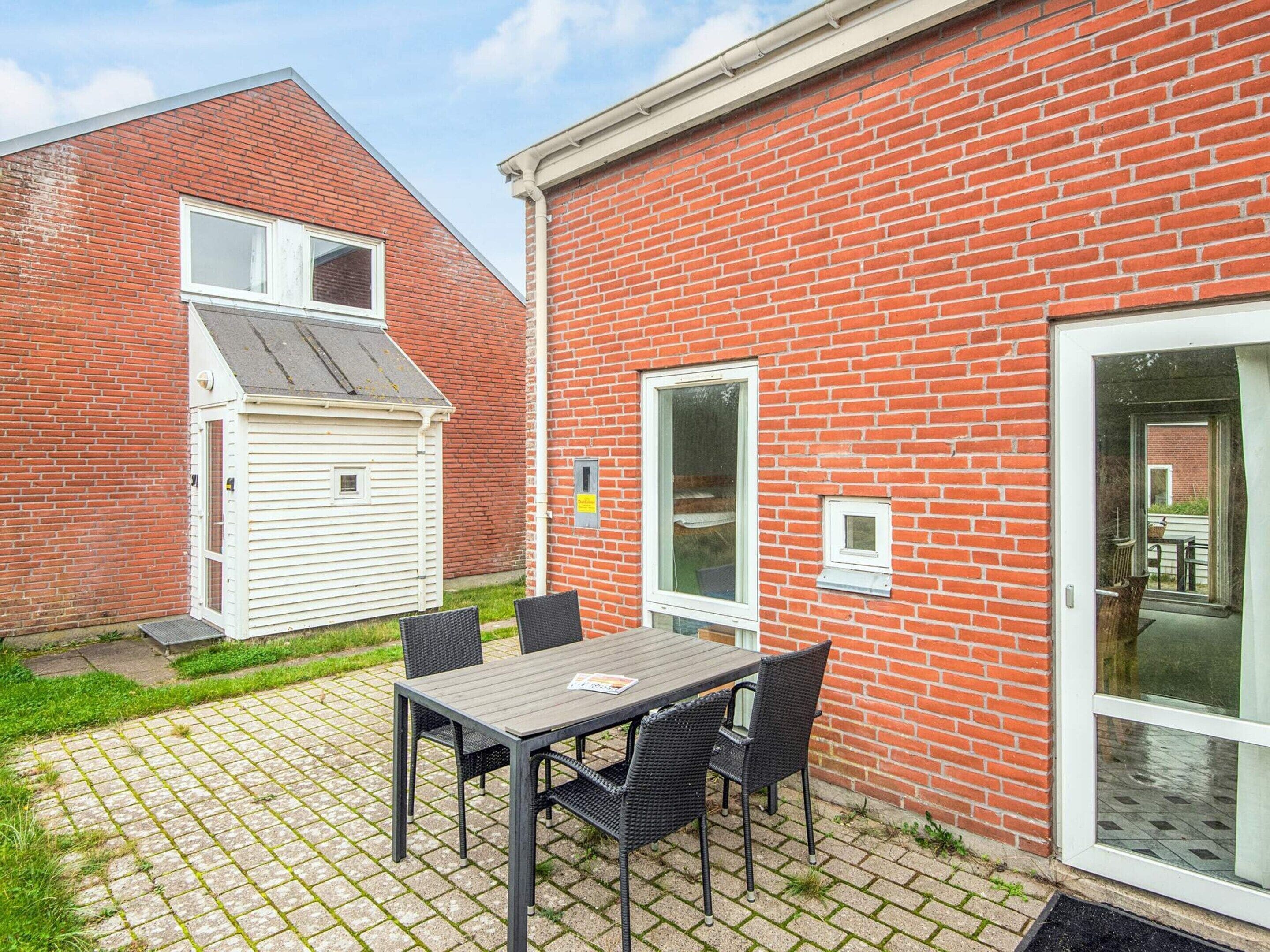 A patio area with a table and chairs, a white shed, and a red brick building with a sliding glass door.