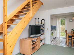 A compact living space with a wooden staircase, a television on a wooden stand, a kitchen area with a dining table, and a view of the outdoors through a glass door. - 6 Person Holiday Home in Romo (Rømø)