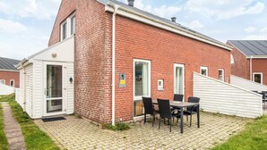 A red brick house with a white door, a small patio with a table and chairs, and a clear sky. - 6 Person Holiday Home in Romo (Rømø)