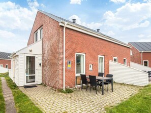 Ett hus byggt av rött tegel med en vit dörr, en liten uteplats med ett bord och några stolar och en klar himmel.