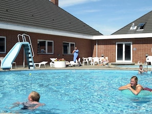 Una piscina con tobogán, sillas de descanso y un edificio de ladrillo al fondo.