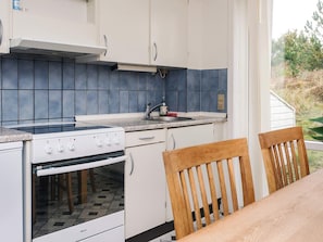 Una cocina compacta con armarios blancos, salpicadero de azulejos azules, estufa y pileta.