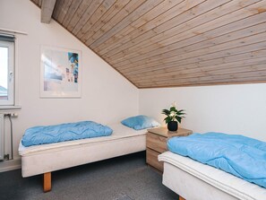 A room with two beds, a window, a radiator, and a wooden ceiling.
