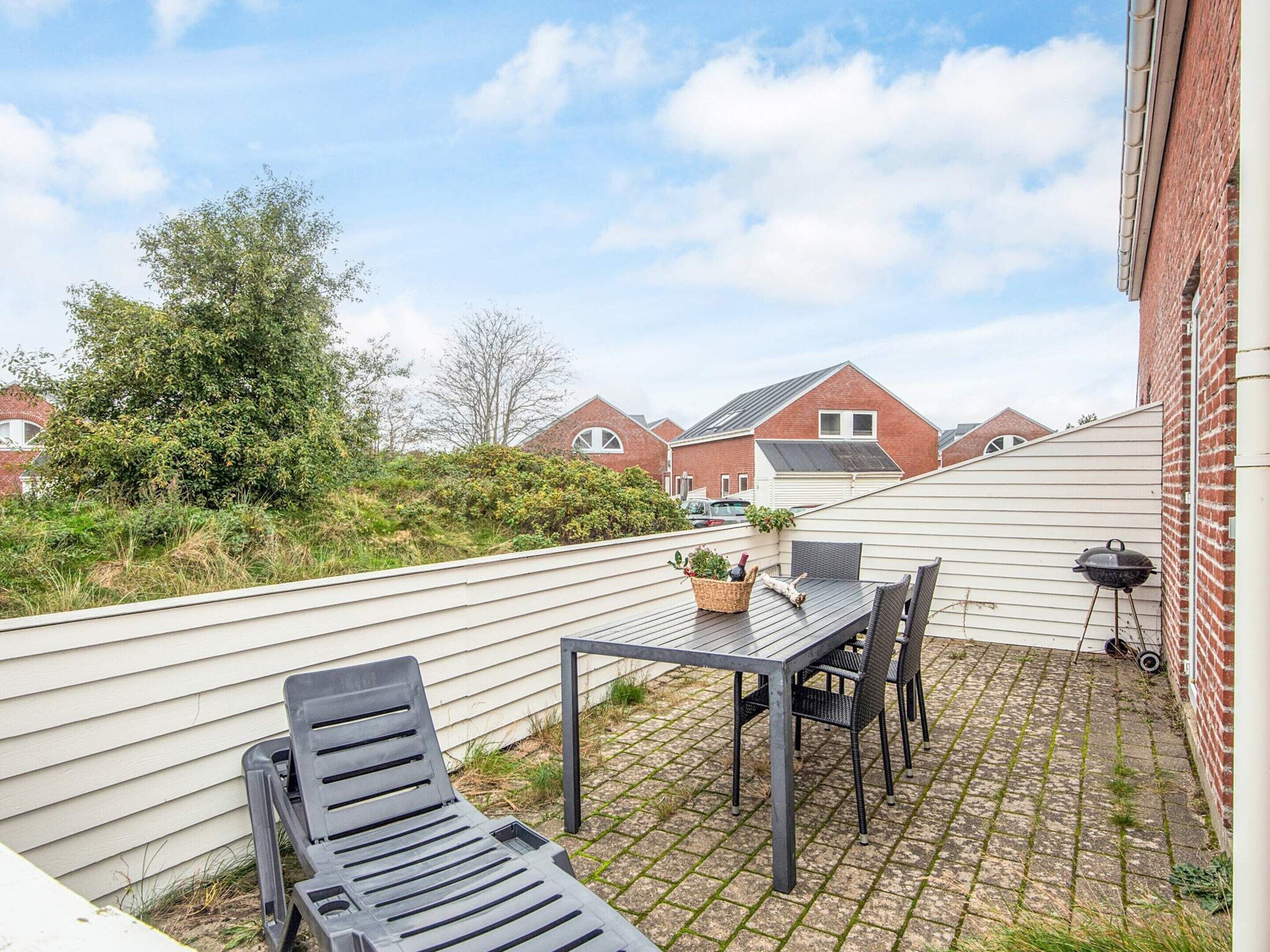 Eine Terrasse im Freien mit Tisch und Stühlen, einem Grill und Blick auf benachbarte Häuser.