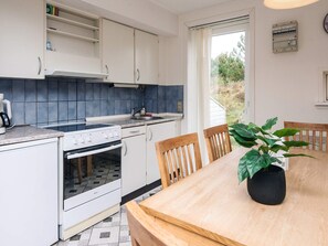 A compact kitchen with white cabinets, a built-in oven, and a sink. There's a dining table with chairs and a potted plant. - 6 Person Holiday Home in Romo (Rømø)