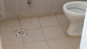 A bathroom with a toilet, a sink, and a floor drain. - Charity Lodge (Nakuru)