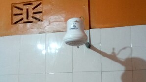 A white ceiling light fixture mounted on a tiled wall with a visible electrical outlet. - Charity Lodge (Nakuru)