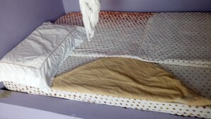 A single bed with a white pillow and a beige blanket. - Charity Lodge (Nakuru)