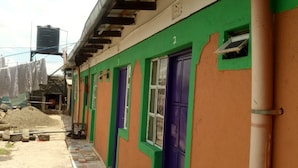 A building with a green and orange facade, multiple doors, and a tiled walkway. - Charity Lodge (Nakuru)
