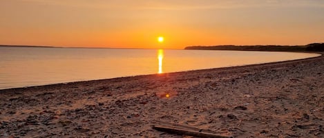 A beach with a sunset, calm water, and a clear sky.