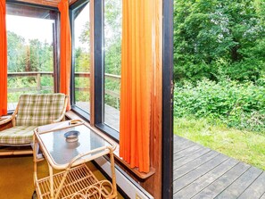 A room with a wicker chair, a small table, and a view of a wooded area through large windows. - Lovely Holiday Home in SpÃ¸ttrup near Sea (Spøttrup)